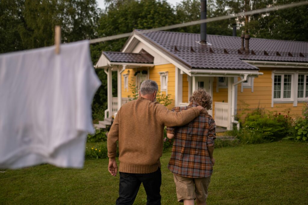 Grandfather and grandson walking together in a lush backyard with a charming house in the background.