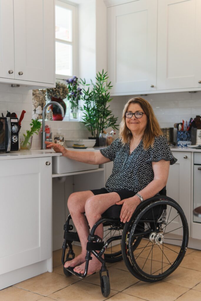 A woman in a wheelchair smiling while in a modern kitchen, conveying accessibility and independence.
